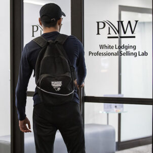 A student stands in front of a door for PNW's White Lodging Professional Selling Lab