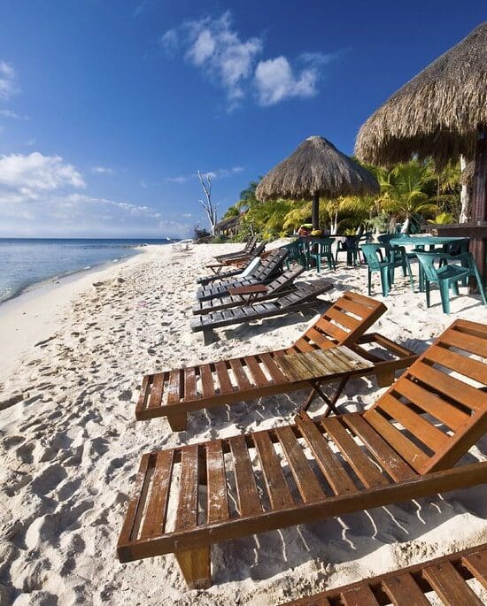 Wooden lounge chairs and straw thatched umbrellas over tables on the beach with a view of the sea and sky