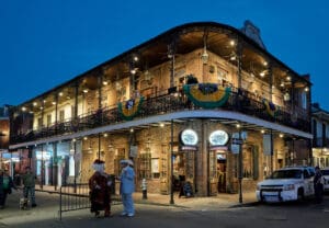 An historic two-story corner building in New Orleans with people chatting in front and people walking a dog.