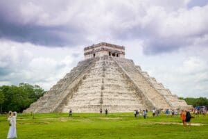 A pyramid in Yucatan with tourists on the lawn and a cloudy sky