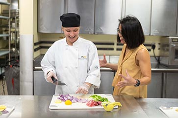 PNW student in HTM and professor talking to one another while student slices vegetables 363x242