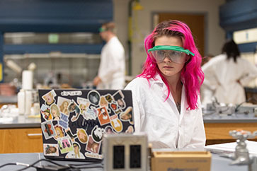 A biology student wearing PPE and a lab coat.