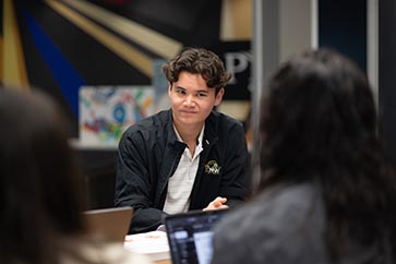 Male student talking with a group of people on campus 1440x600