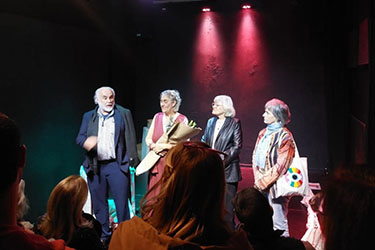 Jose Castro Urioste, Nora Ugartemendia, Maria Ines Martinez, and Graciela Balletti stand on stage in a spotlight.