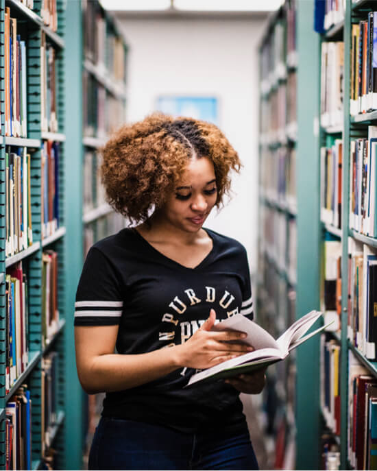 student looking at book in library stacks