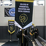 A student carries a College of Humanities, Education and Social Sciences banner
