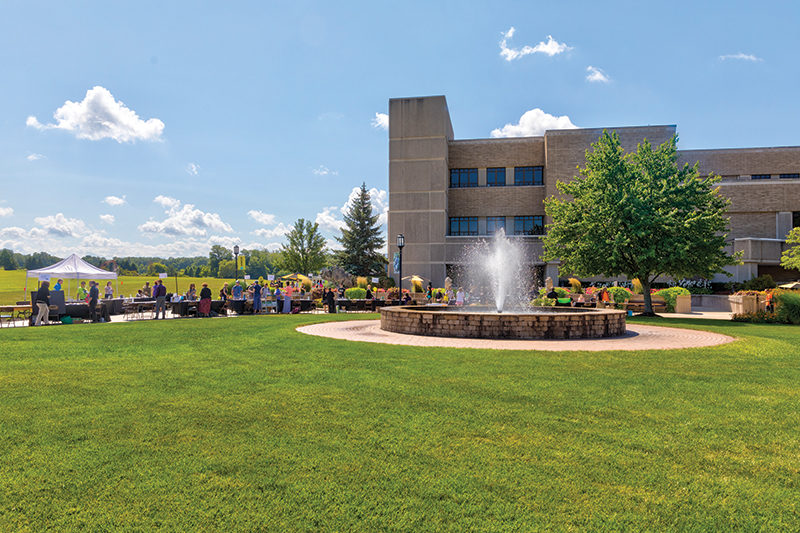 People gather in front of a building and fountain on PNW's Westville campus on a sunny day.