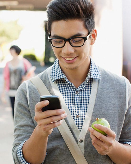 A student texts while holding an apple