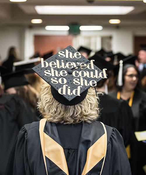 A PNW graduate in a crowd. Her cap reads "She believed she could so she did."