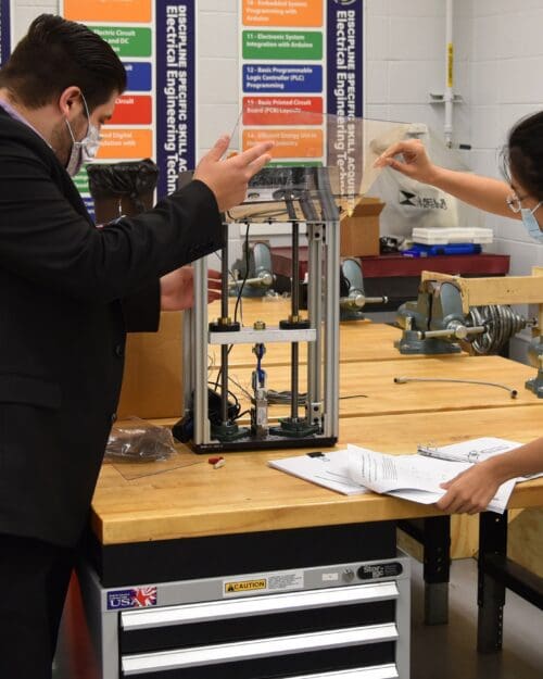 Afshin Zahraee, assistant professor, Mechanical Engineering Technology (left) and Ran Zhou, assistant professor of Mechanical Engineering examine a miniature tensile testing machine for 3D printed parts and specimen for potential use in Remote Knowledge Labs.