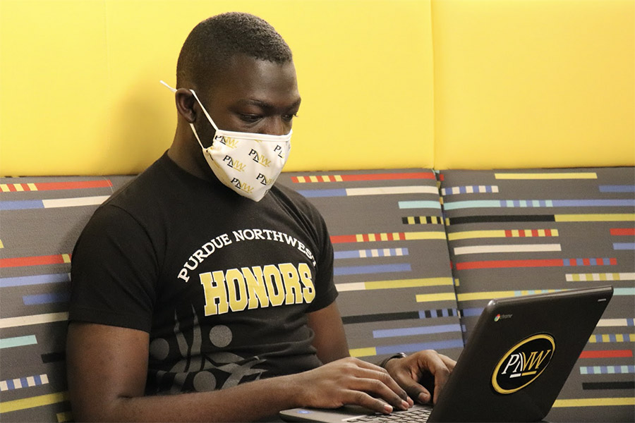 A student in a PNW Honors College T-Shirt wearing a mask works on a laptop