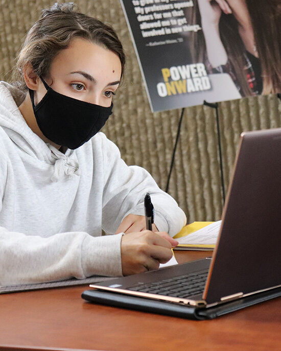 A masked PNW student studies at a laptop computer on campus.