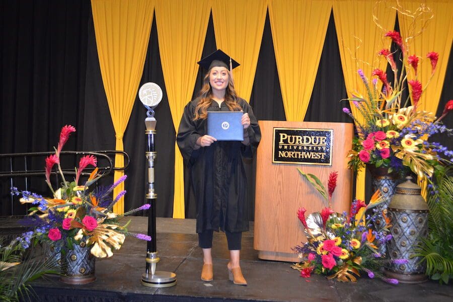 A PNW grad poses with her degree next to a podium