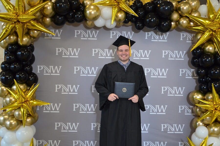 Student is pictured in front of logo and balloons.