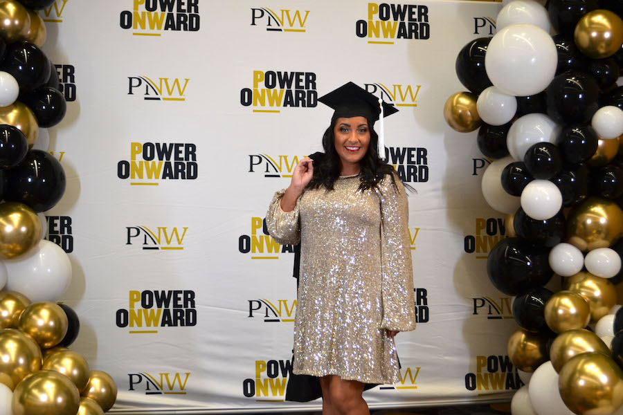 A PNW graduate is pictured in front of the step and repeat.