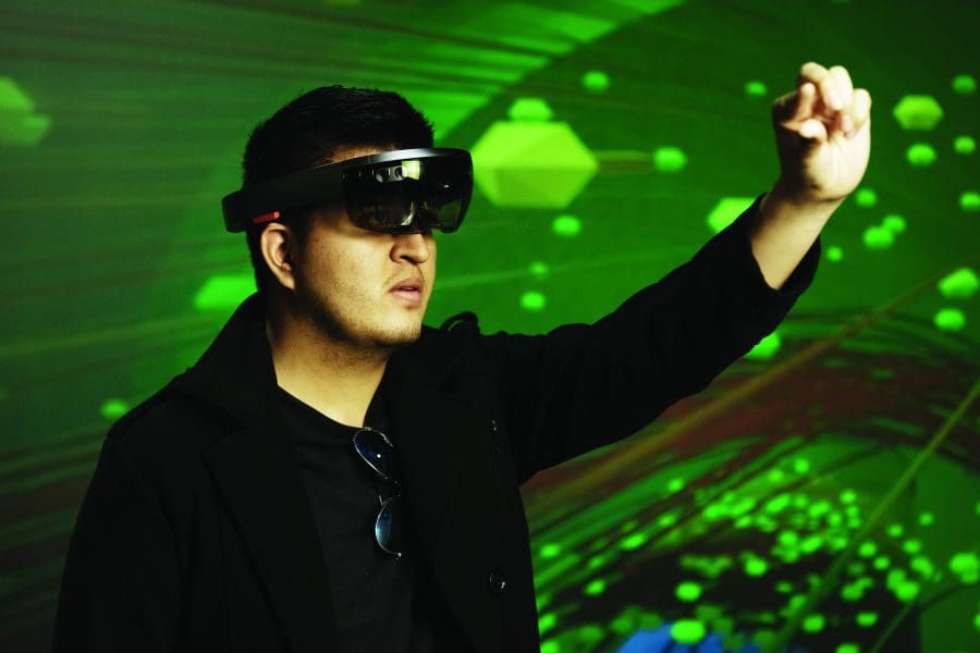 A student wearing goggles stands in front of a green background