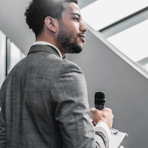 A young man in a gray suit holds a microphone