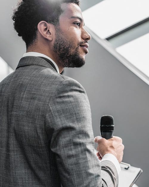 A young man in a gray suit holds a microphone