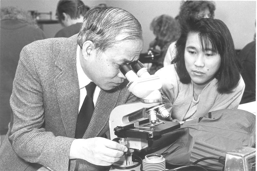 A professor looks through a microscope.