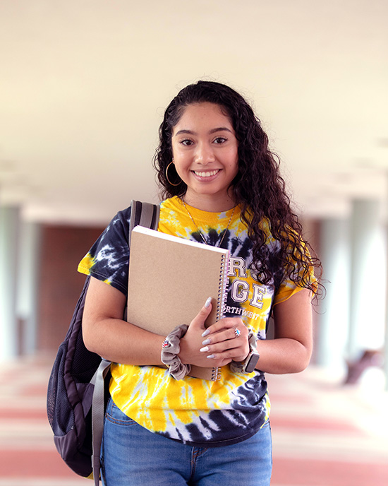 A PNW student in a tie-dye t-shirt holds her notebook outdoors.