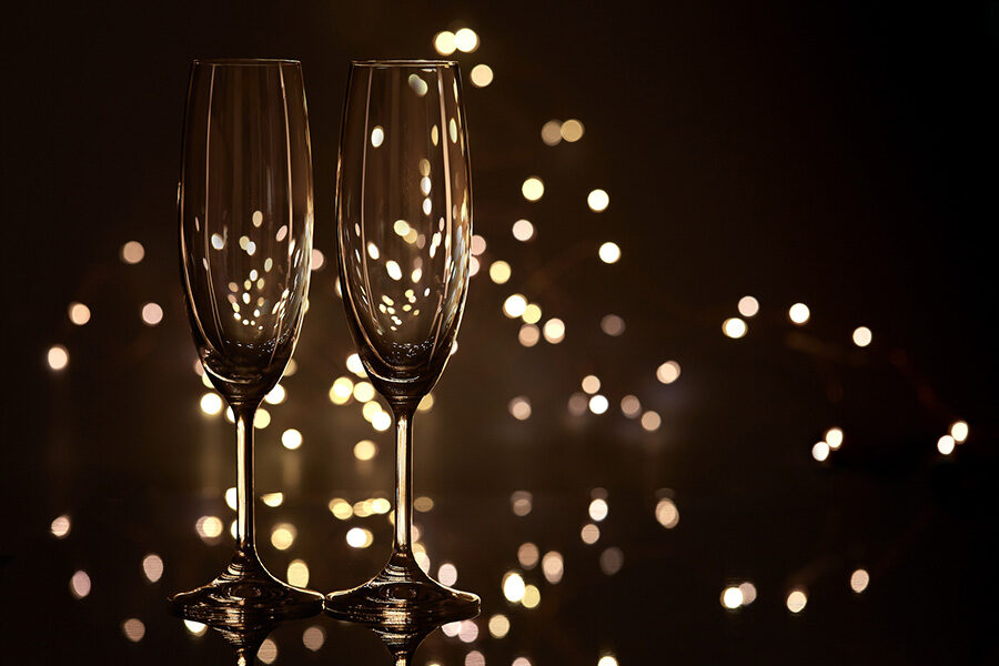 Two empty glasses for champagne on a dark background with LED lights garland. Copy space for text.