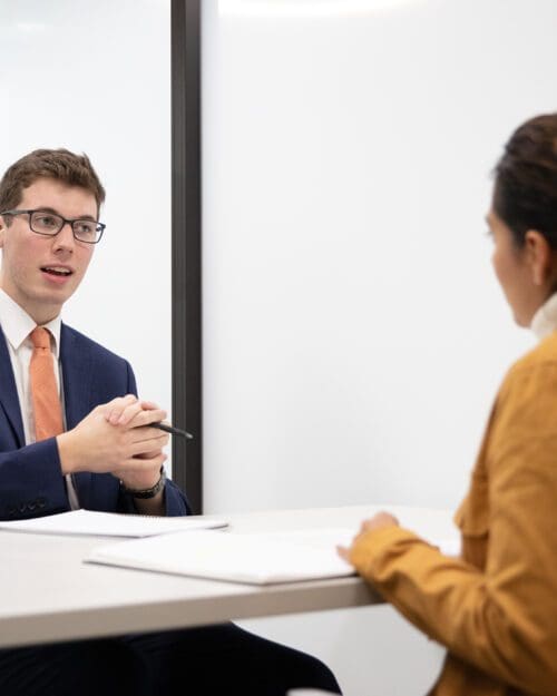 Two students in suits speak over a table.