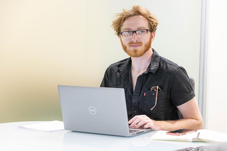 A student in glasses works on a laptop