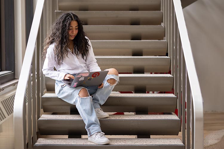 A student works on a laptop in a stairwell