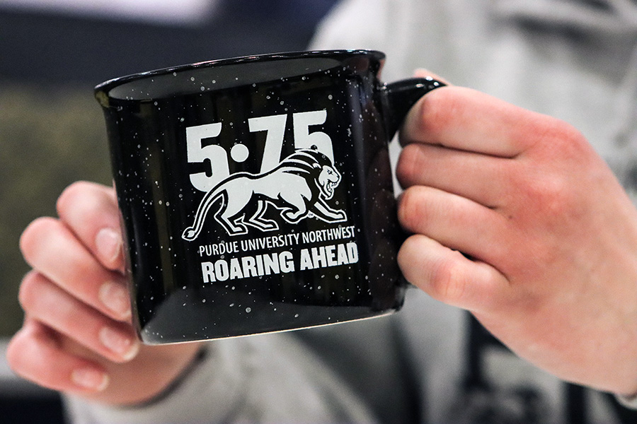 Hands holding a mug with a lion and text reading "5-75 Purdue University Northwest Roaring Ahead"