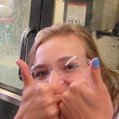 A student in safety goggles gives a thumbs up