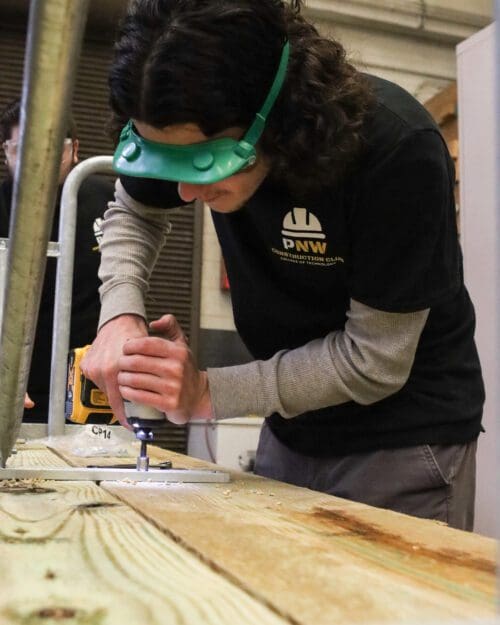 PNW Construction Club president Clayton Whiting drills bolts into the picnic table’s legs to secure them.