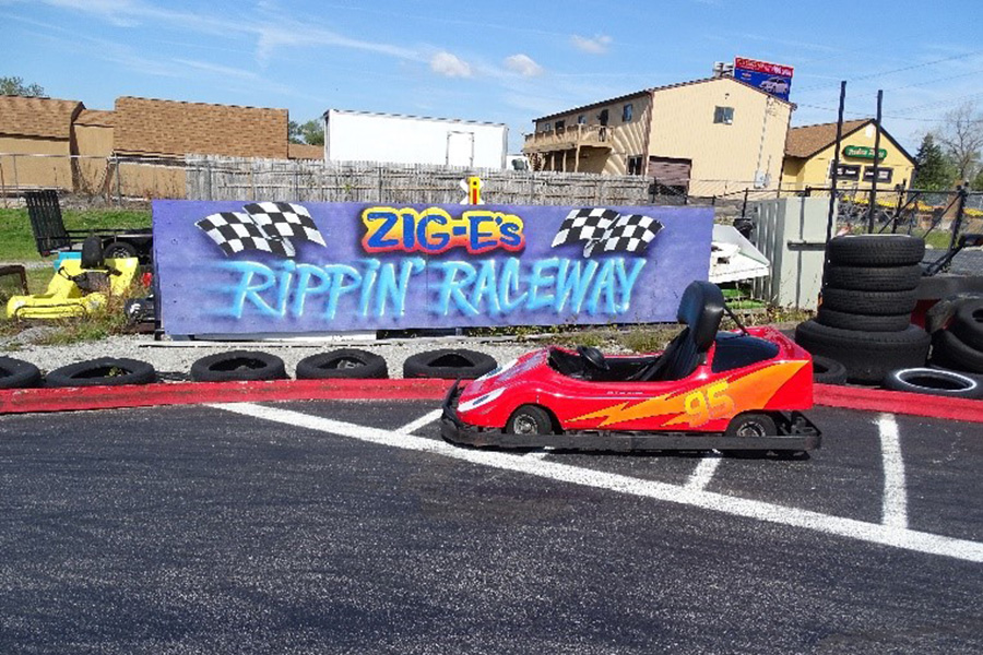 A go-kart sits in front of tires and a sign that says "Zig-E's Rippin' Raceway"