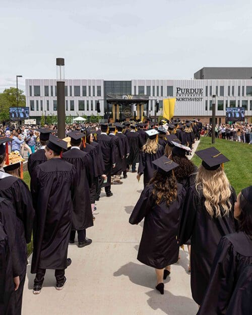 PNW graduates in regalia walk to the Nils K. Nelson Bioscience Innovation Building.