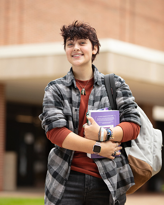 A PNW student holds books outside the Student Union and Library Building