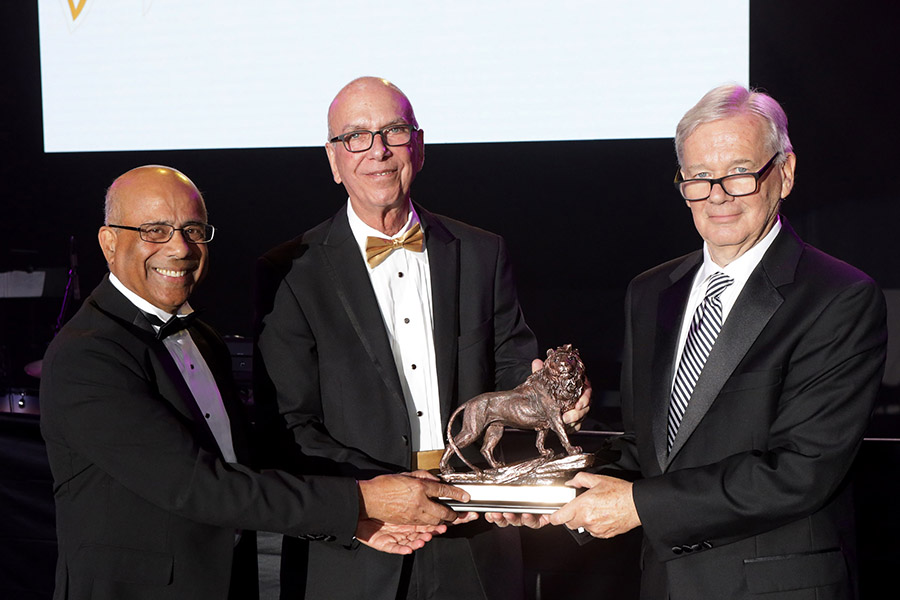 Niaz Latif, Thomas L. Keon, and David Roberts stand smiling while holding the PNW Hall of Fame trophy