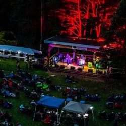 People sitting on a lawn in front of a stage at Gabis Arboretum