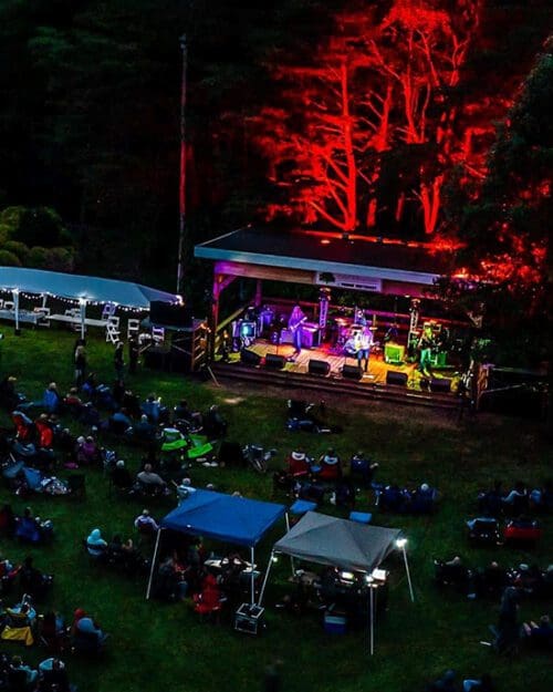 People sitting on a lawn in front of a stage at Gabis Arboretum