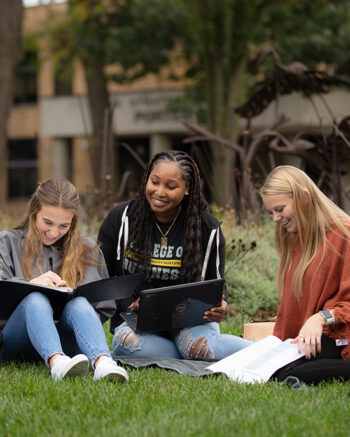 Three students sitting on the grass and studying