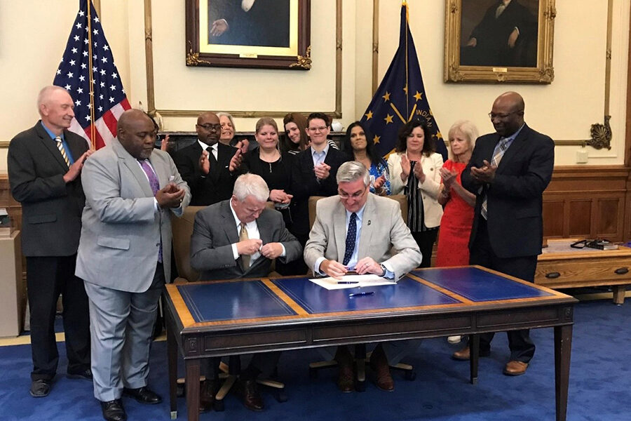 Group of people stand behind Governor Holcomb as he signs HB 1150 bill: Monetary Compensation for Exonerated Prisoners