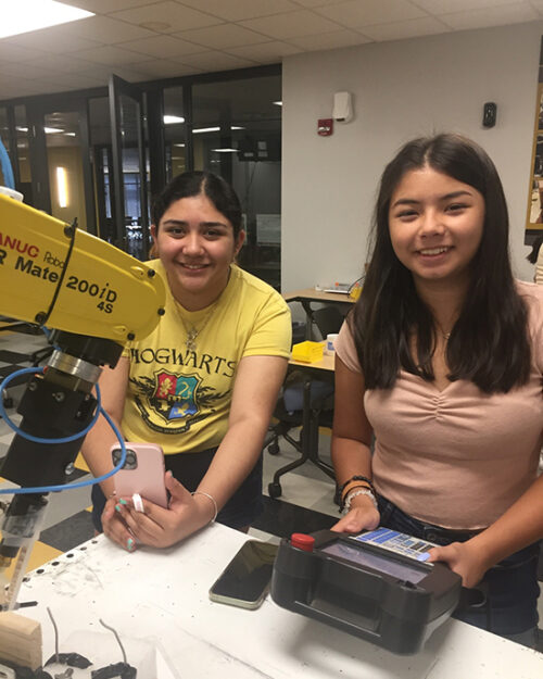 Two students smile next to a robot