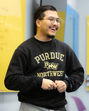 Student smiles while standing in front of a yellow dry erase board