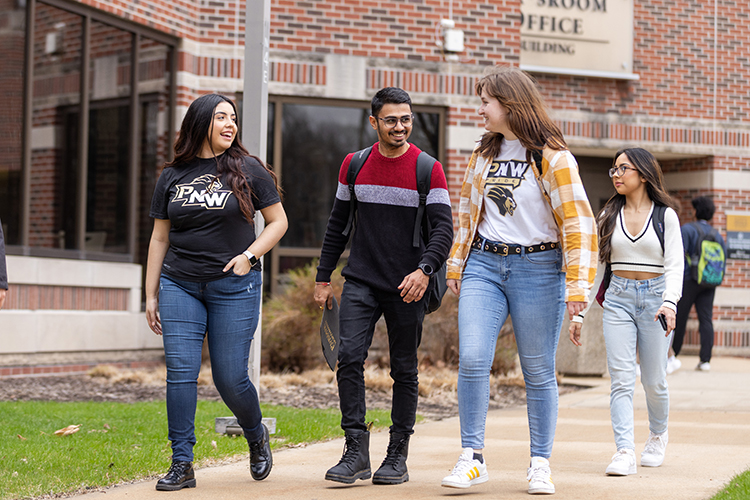 Three students walk together and look at each other. There are two more students in the background