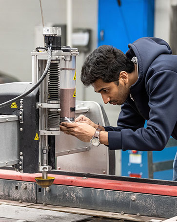 A PNW student bends over machinery