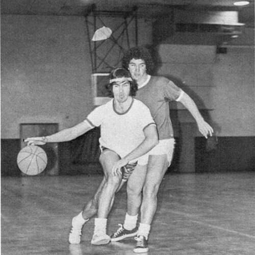 Two students play basketball. The photo is black and white