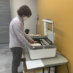 Clayton Whiting stands in front of a laser cutter