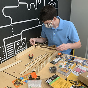 Michael Nickolaou sits at a table and pieces together the wooden supports