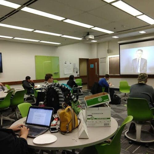 Students sit in a classroom watching a video being projected onto a screen