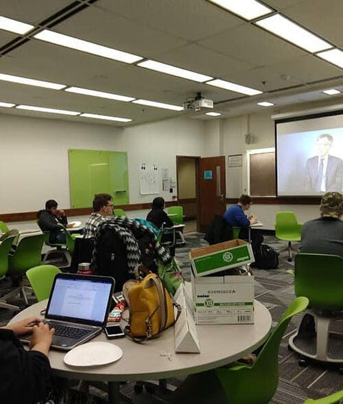 Students sit in a classroom watching a video being projected onto a screen