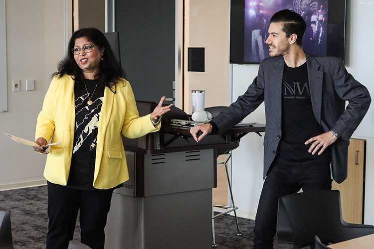 Neeti Parashar stands left of Nathan Elizalde. There is a podium and screen behind them.