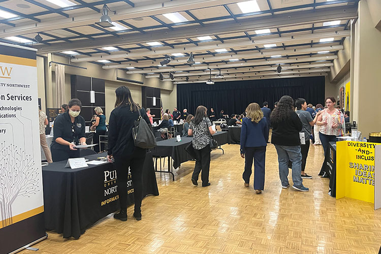 Faculty and staff walk around Alumni Hall where there are tables from departments and resources on campus